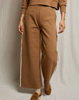 A person wears the Perfectwhitetee Mikos Travel Wideleg Pant in brown with white side stripes, paired with a matching top, beige socks, and brown loafers, standing against a neutral fabric backdrop.