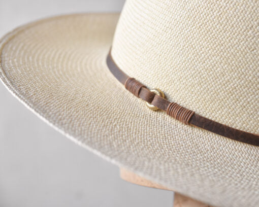 Close-up view of a Ninakuru Theo hat with a brown leather band, photographed in a Scottsdale, Arizona bungalow, on a neutral background, highlighting the texture and detail of the weave.