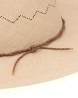 Close-up of a beige Ninakuru Luna hat featuring decorative perforations and a braided leather band tied in a knot. The texture of the hat is detailed and tactile.