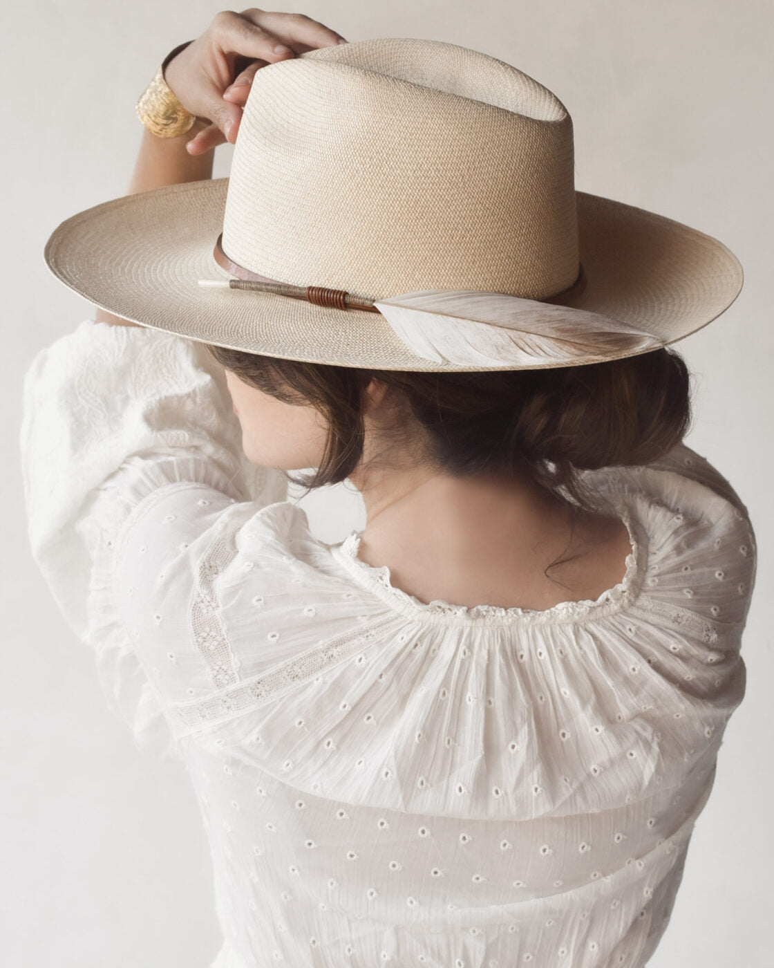 A woman from behind wearing a Ninakuru Matteo XLong Brim made of sustainably harvested Toquilla straw and a white blouse with delicate lace detailing, the focus is on the textures and details of her attire.