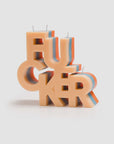 The Mother Burnout F..CKER Candle by Mother features block letters crafted from beige, red, and blue soy wax with five wicks, shown on a plain white background.
