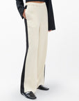 A person wears Rag & Bone's olivia stripe pant—cream with black side stripes—paired with a black long-sleeved top and shiny black shoes, creating a sporty look against a plain white background.