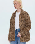 A woman with short blonde hair models the Pistola Cecile Quilted Jacket in leopard print over a white t-shirt and blue jeans, standing against a plain light background.