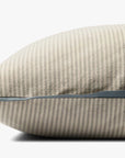 A close-up side view of the PJBR0001 Natural BB Pillow by Loloi Rugs, featuring beige and light gray stripes with blue piping, made from 100% cotton and a hidden zipper, shown on a plain white background.