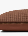 A close-up side view of the Loloi Rugs Rust Pillow 12x27, featuring brown quilted faux leather and a gold zipper closure, set against a plain white background.
