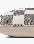 A close-up side view of the Loloi Rugs Checkered Pillow 22x22 displays its textured black and white checkered top with a plain beige bottom.
