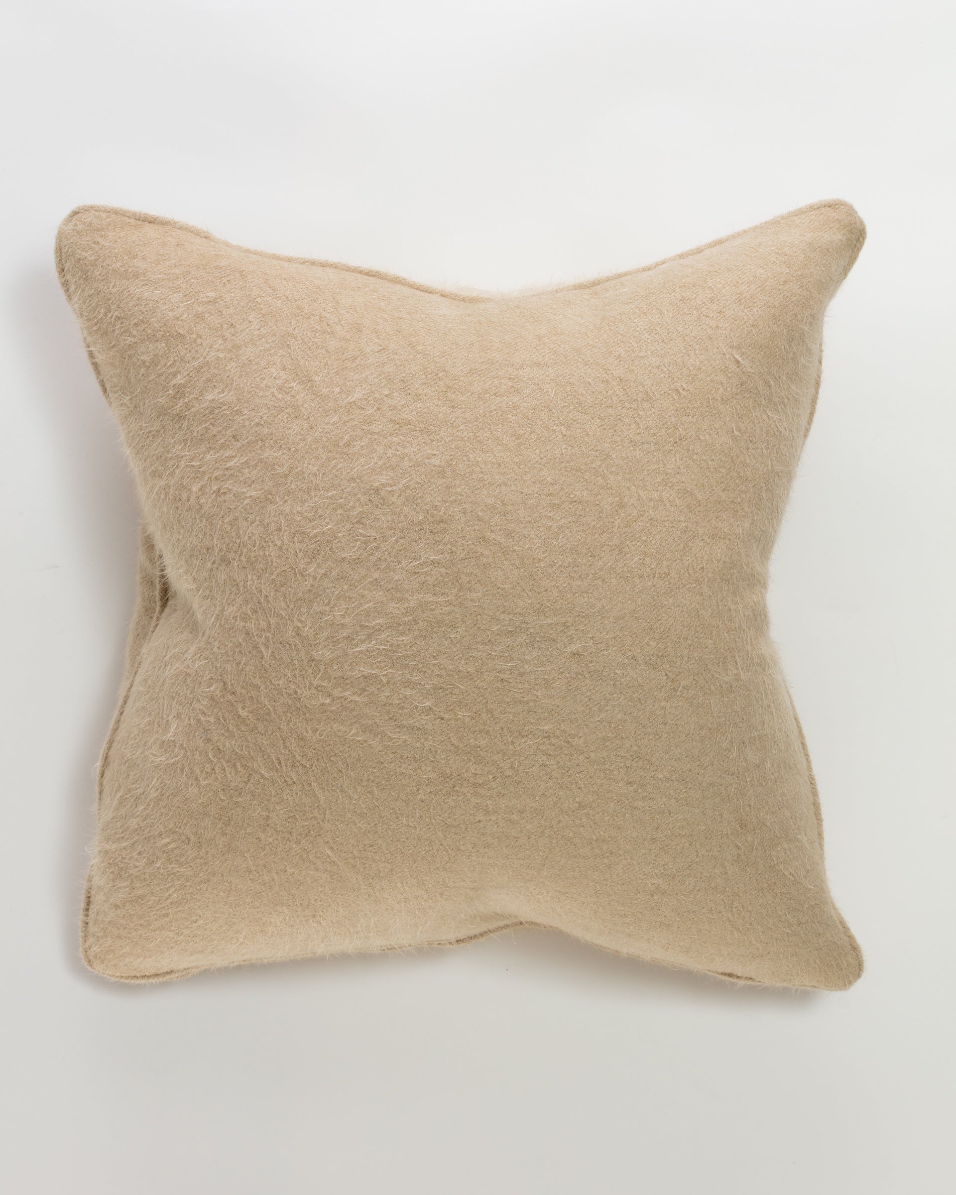 The Massoud Cuddles Sand Pillow 26" is a square, beige pillow with a soft, fuzzy texture and luxurious down feather insert. Its slightly creased surface radiates plush comfort, elegantly complementing a neutral white backdrop.