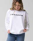 A person in the Faire FREEDOM Charlie Kirk Sweatshirt, featuring bold black "FREEDOM" lettering, stands against a plain background looking down and softly holding the hem—capturing conservative activist Charlie Kirk's spirit.