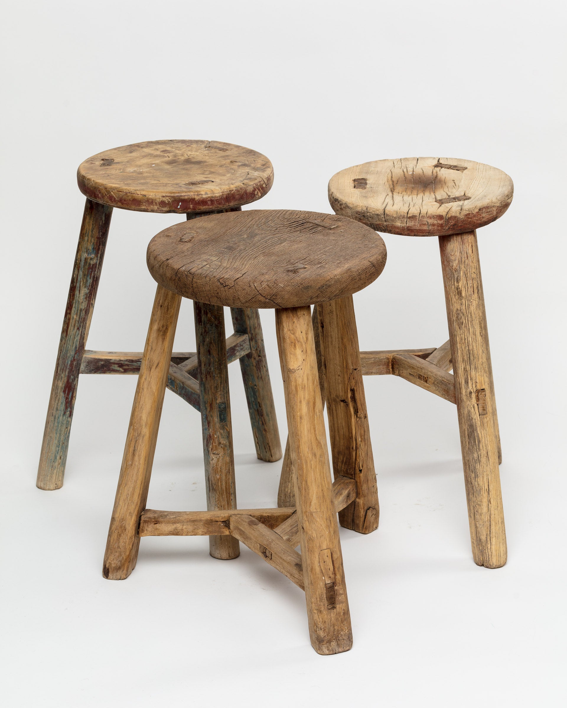 Three ROUND STOOL 48 from Indus Design Imports with varying heights and weathered textures against a white background. Each stool from a Scottsdale Arizona bungalow features unique paint remnants and natural wood patterns.