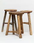 Three ROUND STOOLs by Indus Design Imports, each of different heights, are arranged closely together against a plain white background. These imported handmade vintage stools feature weathered surfaces with visible grain and wear, highlighting their artisan craftsmanship and imparting a timeless elegance.