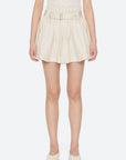 A person wears the Sea New York Angelina Suiting Flare Short—high-waisted, pleated, with an elastic waistband and belt—paired with a cream textured sleeveless top and matching cream flats, standing against a plain light background.