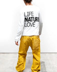 A person faces away on a concrete floor against a white wall, wearing the Free City Out of Sight Poplin Jump Pant by sparrow, LLC in yellow, paired with a white Japanese poplin shirt, olive green boots, and a black beret.