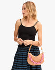 A woman in a black camisole and blue-striped skirt holds a Clare Vivier Shortie Strap Q1 bag with a vintage brass chain, looking left against a plain light background.