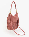 The Clare Vivier Petit Moyen Messenger Suede Fringe is a pink suede mini bag with gold hardware, top handle, crossbody strap, and fringe on the sides and bottom, displayed against a white background.