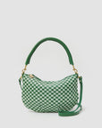 The Clare Vivier Petit Moyen Messenger S25 rests against a plain background, displaying a green and white checkerboard pattern. It features a curved green handle, detachable crossbody straps, handwoven leather accents, and gold-tone hardware.