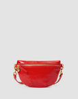 The Clare Vivier Petit Fanny F25 is a shiny, bright red patent leather crossbody bag with a textured finish, gold-tone zipper and hardware, rounded shape, and detachable strap, shown against a plain light gray background.