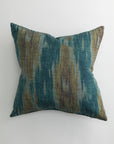 The RANDERS 26x26 Pillow by Pindler features a textured fabric cover with an abstract teal, blue, brown, and gray pattern. Shown on a white background, it includes a plush down feather insert for comfort.