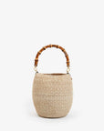The Pot de Miel basket bag by Clare Vivier, featuring a woven straw texture and rounded shape with a bamboo handle, is showcased against a plain white background.