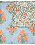 The Bipin Tangerine Quilt by John Robshaw is a hand-quilted cotton voile throw, showcasing large orange flowers and green leaves on blue and white stripes, with a reverse of small red and yellow blossoms on white.