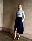 Rachel Comey Sobre Skirt in blue, styled with a turtleneck and red heels against a textured wall.