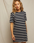 A striped beauty with wavy blonde hair models the Rhett SS Tee Dress by Perfectwhitetee—a short-sleeved, navy blue and white t-shirt dress—against a plain light backdrop.