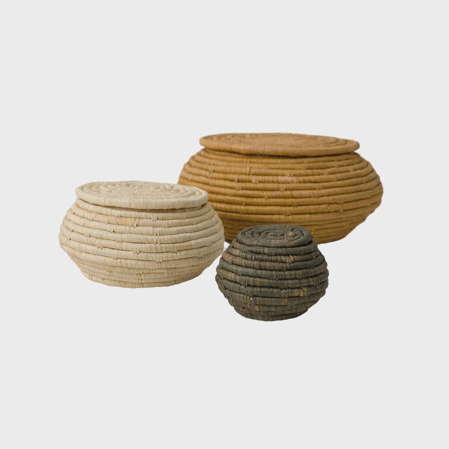 Three Town Square Lidded Woven Boxes of different sizes and colors, reminiscent of the crafts found in a Scottsdale, Arizona bungalow, are isolated on a white background. The boxes feature tightly woven designs, with the largest being light brown, the medium tan, and the smallest dark brown.