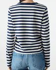 A person with long dark hair, seen from behind, wears the AMO Denim Brigitte LS Tee in navy and white stripes with blue jeans against a plain light background.