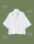 The ROSIE SS Button Up F25 by Frank & Eileen is a white, short-sleeve button-up with an oversized, cropped fit, split seams, side slits, and a stepped hem, shown on an olive green background with labels.