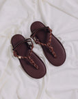 Flowze FLO Sandals—comfortable brown leather sandals with braided straps—are displayed on crumpled white fabric.