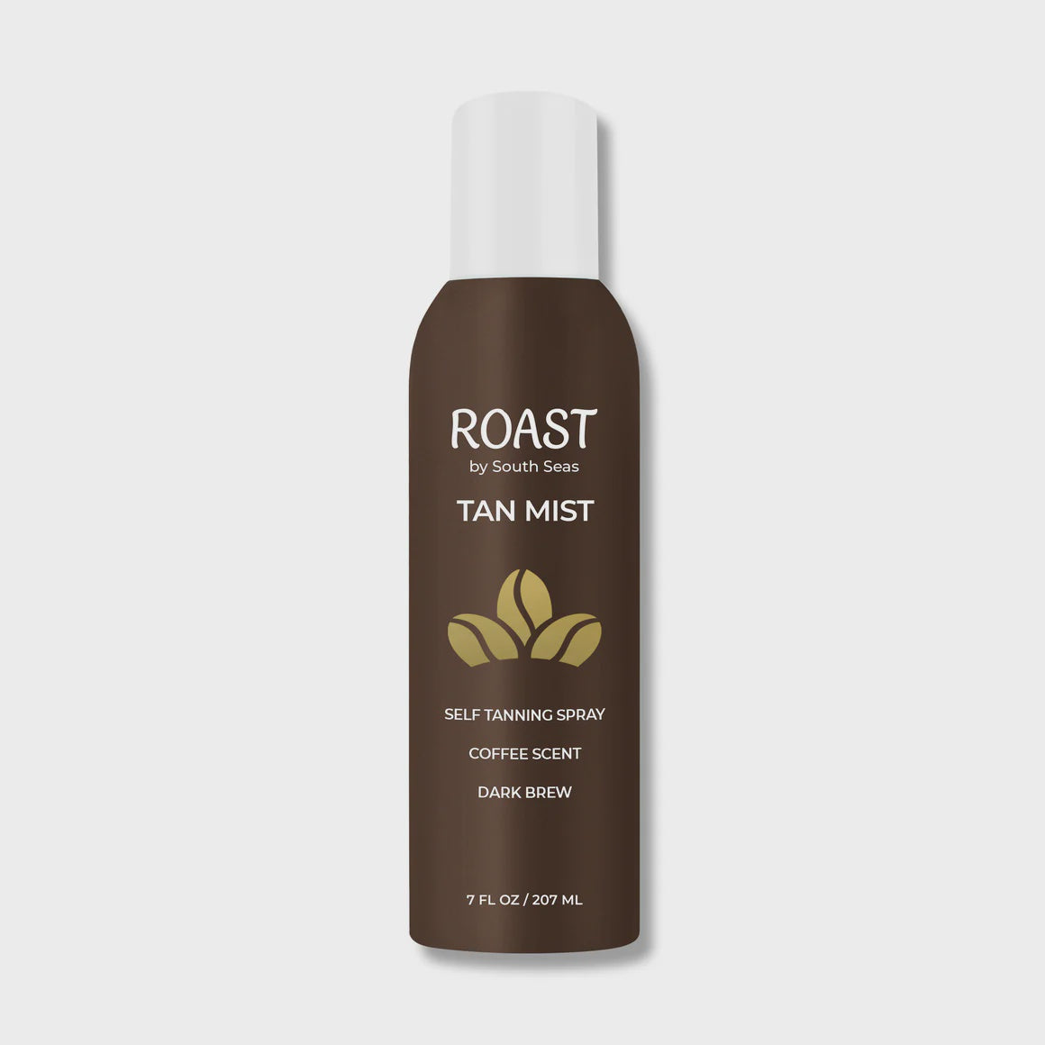 A bottle of "Roast Dark Tan Mist by South Seas Skincare" self-tanning spray with a coffee scent is displayed against a white background in a Scottsdale, Arizona bungalow. The bottle is brown with a white label and a green coffee bean icon.