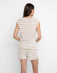 A woman with long brown hair, seen from behind, wears the Lisa Todd Summer Lovin Sweater—a beige and white striped tank top romper with a crochet heart detail—standing against a plain white background.
