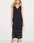 A woman stands against a white background wearing Lisa Todd's Best Dressed sleeveless black V-neckline maxi dress with mesh hem inserts, paired with black sandals.
