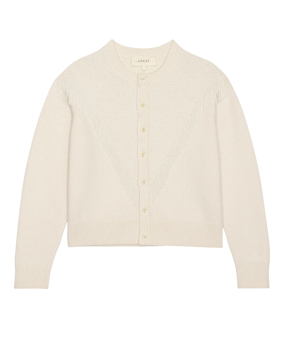 The Beaded Fringe Cardigan by The Great Inc. is a cream-colored, long-sleeve wool-cotton blend with ribbed hem and cuffs, a subtle V-shaped front texture, and matching buttons, inspired by classic 1930s rodeo sweaters.