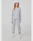 A person stands against a plain background in Kule's Women's Organic Sweatpants and a light gray sweatshirt. Complementing their relaxed pose are white sneakers and a white bucket hat, enhancing the laid-back vibe. The outfit is practical and stylish, being entirely machine washable.