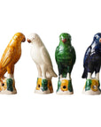 Blue Ocean Traders' Parrot Small features four hand-painted ceramic bird figurines—yellow, white, green, and blue—each perched on decorative bases with leaf patterns, inspired by Jingdezhen porcelain.