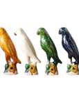 Blue Ocean Traders' Parrot Small figurines, inspired by antique reproductions, feature four ceramic parrots—yellow, white, green, and blue—perched in a row on decorative bases accented with yellow and green.