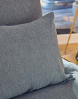 A close-up of the Toro Canyon Org, Euro Sham Marine by Coyuchi Inc on a bed with matching bedding, beside a wooden nightstand holding a tray and bottle. Sunlight highlights its mid-century textile artist-inspired weave.