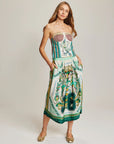 A woman with long light brown hair wears the Me369 Vanessa Midi Skirt, a colorful viscose midi with green and gold designs and an elastic waist, paired with a strapless patterned bodice and gold flats.