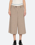 A person wears Sea New York's Savannah Plaid Culotte with a wide-leg fit, a white patterned sleeveless top, black lace-up shoes, and a visible boxer-style waistband featuring text, set against a plain light gray background.