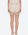 A person faces away wearing Ethel Solid Shorts by Sea New York in cream, featuring a lace hem and patterned elastic waistband, paired with cream slip-on shoes and a textured sleeveless top, set against a plain white background.