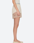 A person stands in profile wearing Sea New York Ethel Solid Shorts, featuring an elastic waistband and scalloped edges, paired with beige Mary Jane shoes against a plain light background.