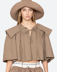 A woman models a sun-ready look with the Lois Twill Hat by Sea New York, styled with a loose tan blouse featuring a square collar, matching tan pants, and a white waistband.