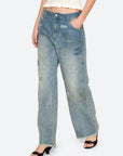 A person wearing Sea New York's Claira Mended Jeans—relaxed fit, wide-leg, light-wash with patchwork and raw hem—styled with a textured white crop top and black open-toe heels.