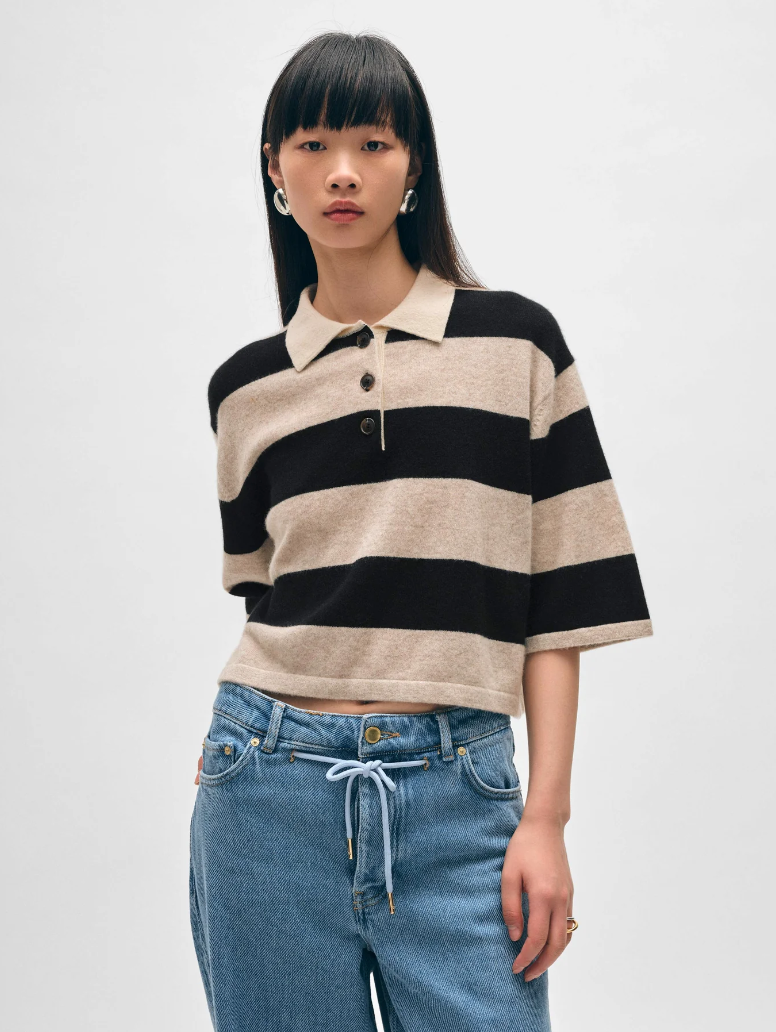 A young woman with straight black hair wears a Cashmere Crop Striped Polo in Sandwisp/black by White + Warren and blue jeans, standing against a plain background in Scottsdale, Arizona. She has large earrings and a calm expression.