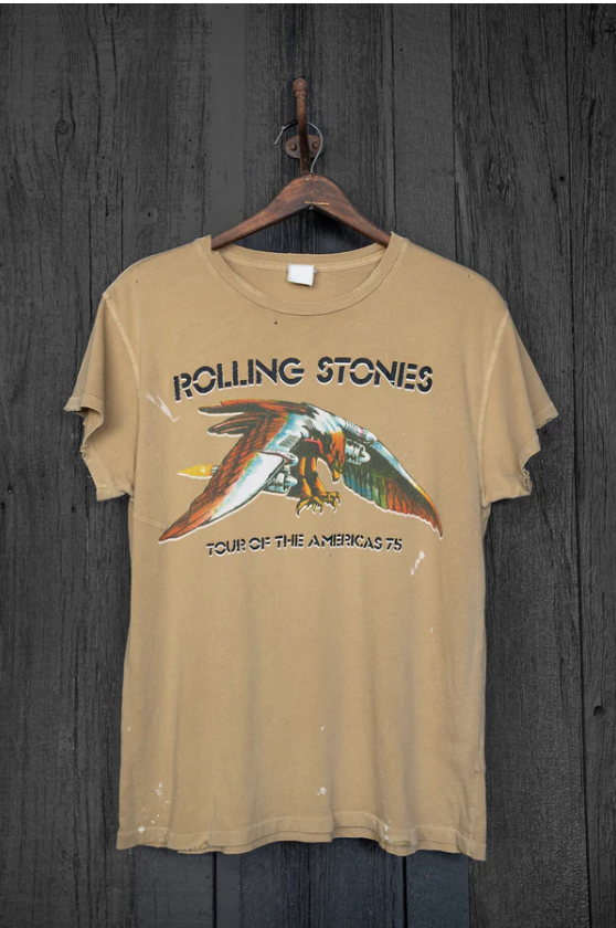 A vintage unisex fit Made Worn Rolling Stones Americas '75 Tour band t-shirt, featuring an eagle graphic, hanging on a wooden hanger against a rustic gray wooden background.