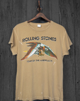 A vintage unisex fit Made Worn Rolling Stones Americas '75 Tour band t-shirt, featuring an eagle graphic, hanging on a wooden hanger against a rustic gray wooden background.