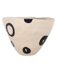 The Clyde Bowl by The Import Collection is a beige porcelain piece with an uneven rim, featuring bold black circles and ovals across its surface—a uniquely detailed design.