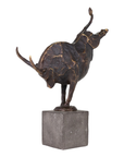 The Import Collection Bull Statuary is a dynamic, abstract bronze sculpture with exaggerated curves and raised horns, balanced on one leg atop a square stone base—perfect for unique home decor.