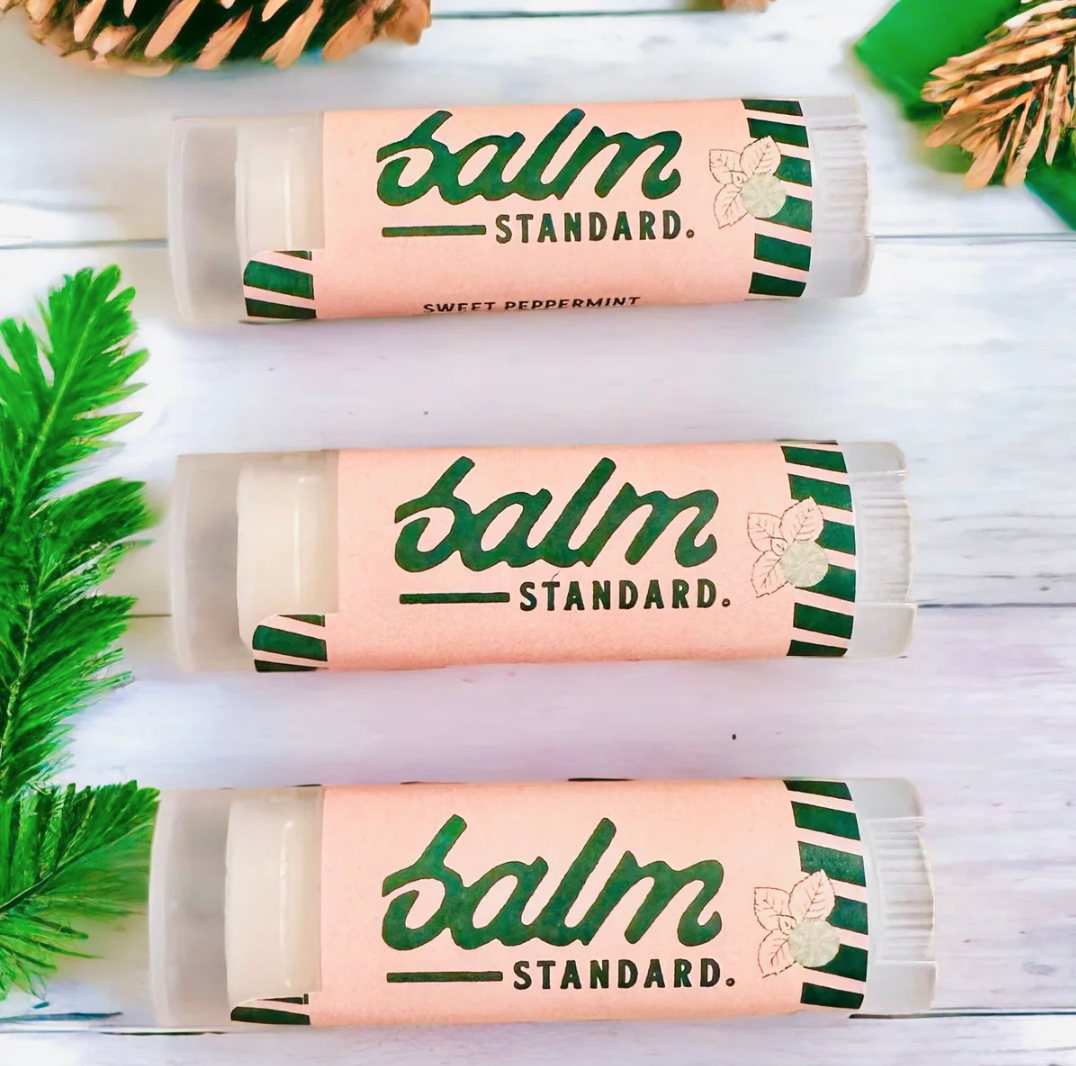 Three Faire lip balms in sweet peppermint design, displayed among pine branches on a light wooden background in Scottsdale, Arizona.