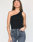 A woman wearing a Perfectwhitetee Call Me One Shoulder Structured Rib Tank and blue jeans stands confidently against a plain white background in her bungalow. Her hand rests on her hip, and she has a relaxed expression with bangs framing her face.